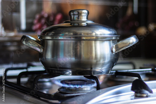 Close-up of a stainless steel pot standing on a kitchen stove with a gas burner on.