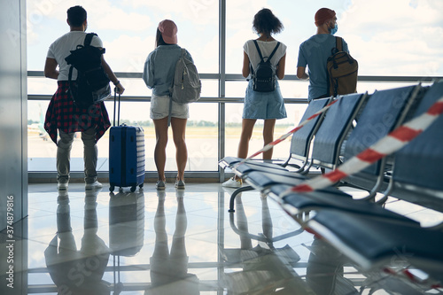 Four people in casual clothes looking out the window while waiting catch a flight
