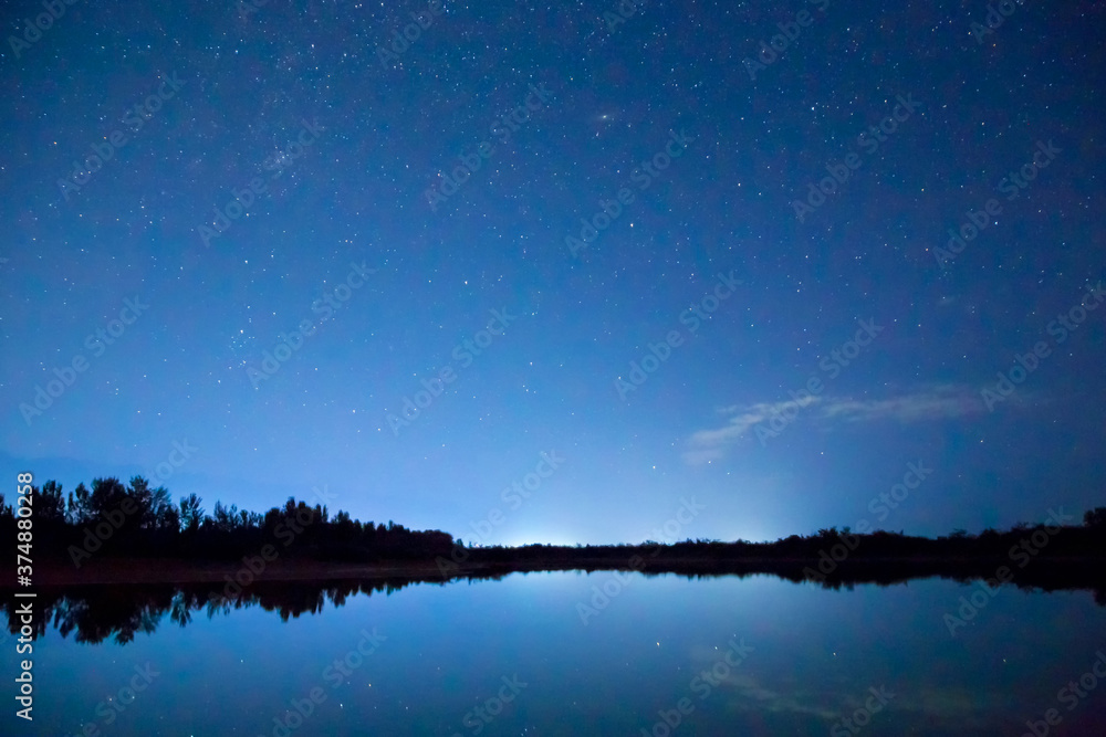 Starry sky and clouds. Night landscape, reflection of star paths in calm lake water. Natural background Starry sky and clouds. Night landscape, reflection of star paths in calm lake water. Natural background