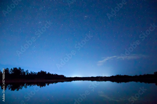 Starry sky and clouds. Night landscape, reflection of star paths in calm lake water. Natural background