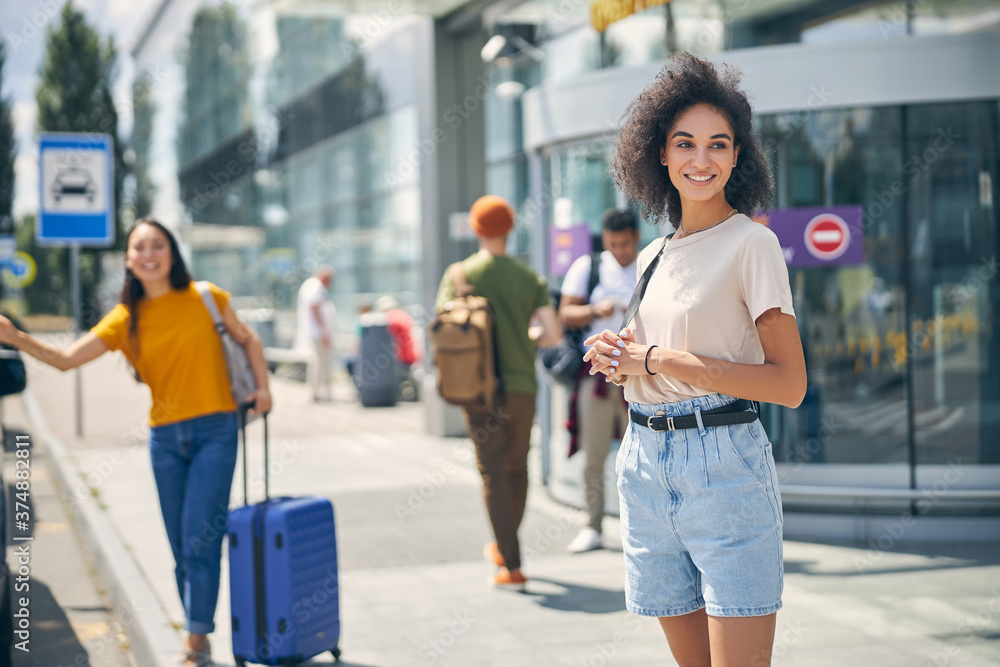 Stylish woman in denim shorts and shirt with backpack on shoulder waiting for a taxi in the outdoors