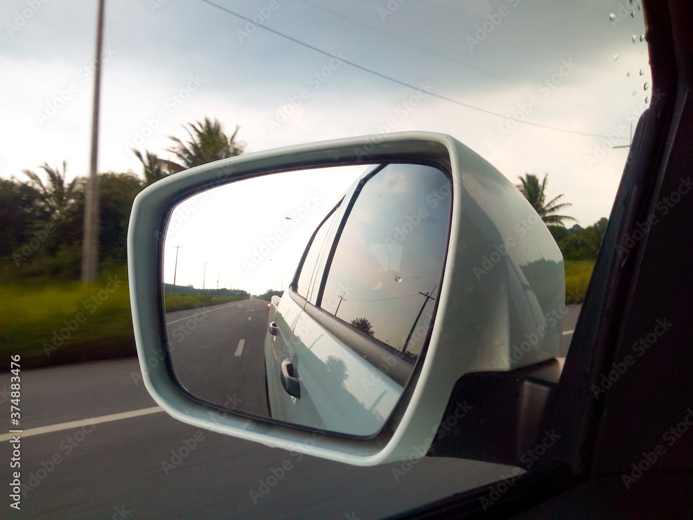 Naklejka premium The view in the car side mirror When the weather is closed, the rain is about to fall in the rural roads of Thailand.