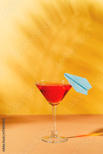 Vacation red cocktail in martini glass with blue paper plane  on yellow background