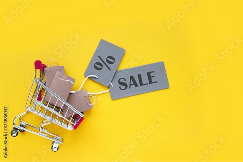 Mini shopping cart with small craft bags and gray labels with an inscription SALE on a yellow background.