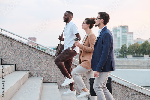 Obraz na plátně Side view of confident multi-ethnic students chatting and moving up stairs while