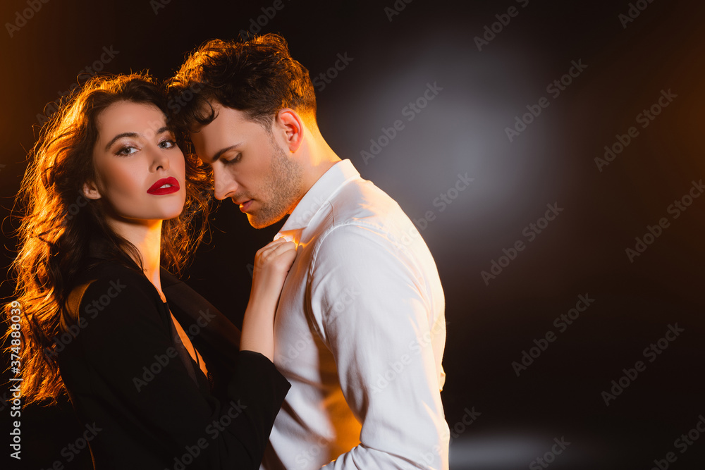 Obraz premium curly woman in jacket touching shirt of man on black