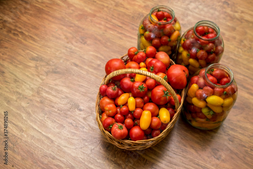 In the photo there is a basket with tomatoes. Fresh organic food from the garden. In the background are jars of canning for the winter.