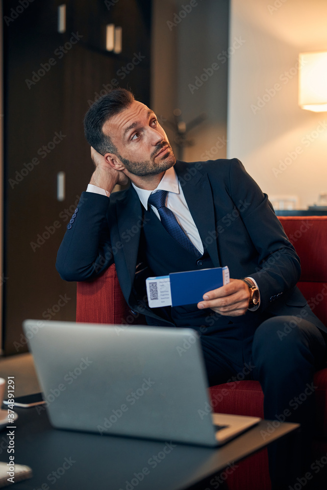 Thoughtful man sitting with his ticket in the airport lounge room Thoughtful man sitting with his ticket in the airport lounge room