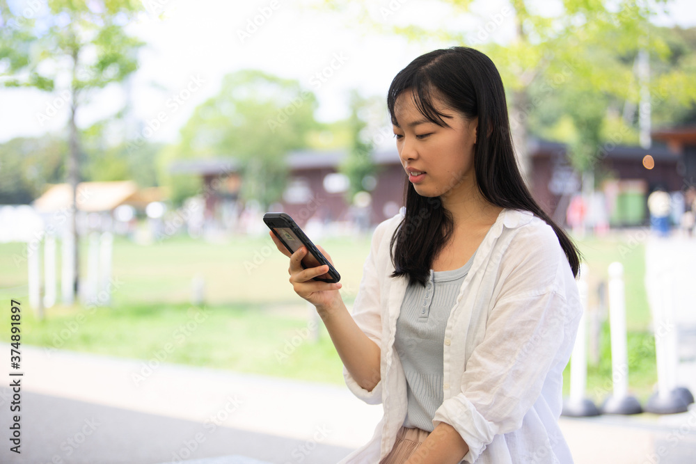 公園でスマホを使う若い女性 公園でスマホを使う若い女性