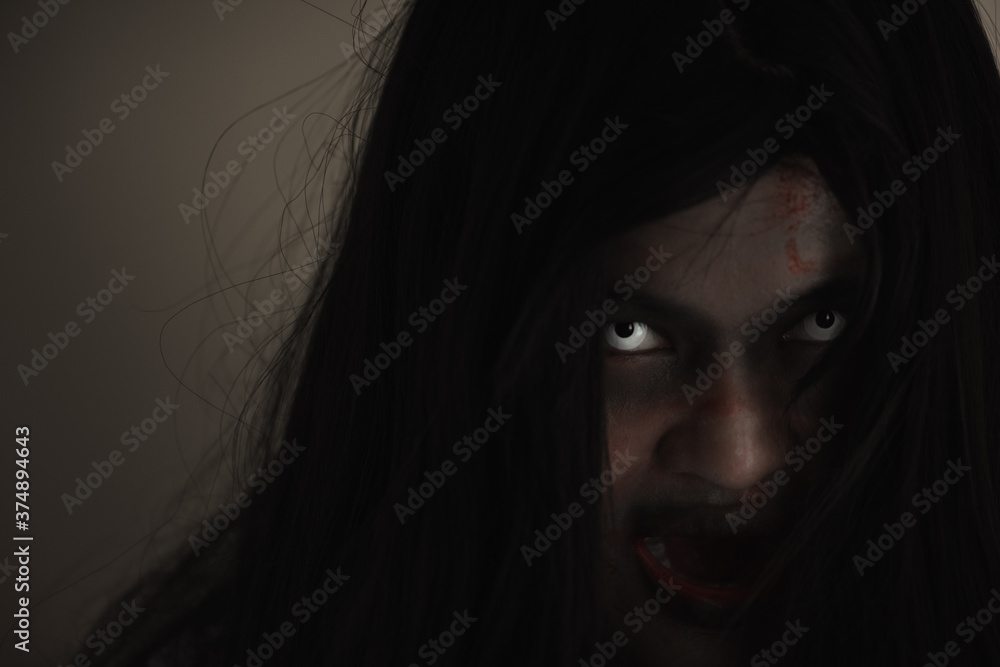 Girl zombie in blood. Closeup face and eyes of Asian Woman ghost with blood. Horror creepy scary fear in a dark house. Hair covering the face, Halloween festival concept