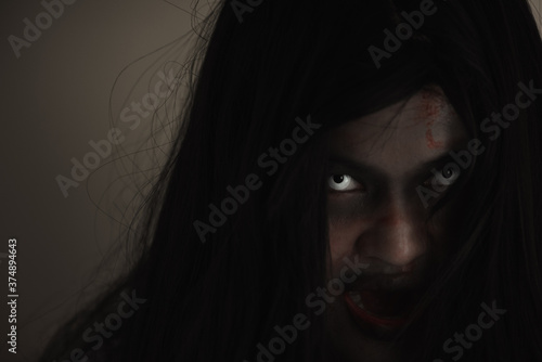 Girl zombie in blood. Closeup face and eyes of Asian Woman ghost with blood. Horror creepy scary fear in a dark house. Hair covering the face  Halloween festival concept