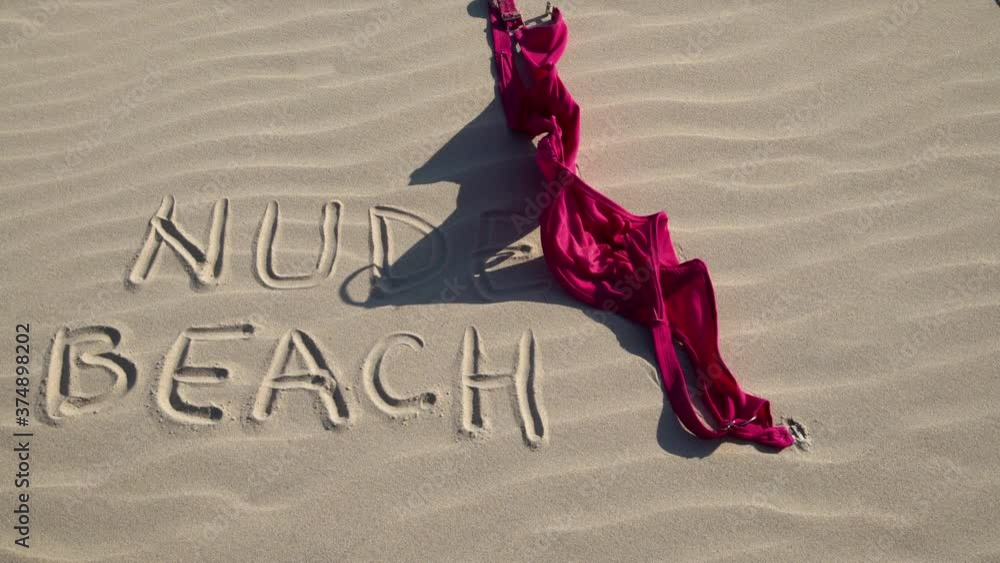 Close up of woman throwing bra at nude beach sign written on sand