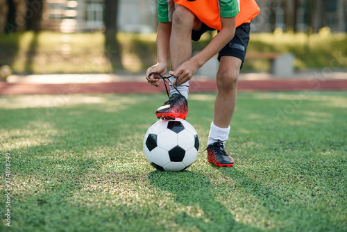 Close up boot of football player which puts his leg on ball and tying shoelace on soccer stadium on the training.