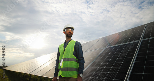 Portrait of electrician in safety helmet and uniform on background field of photovoltaic solar panels. Male technician at solar station. photo