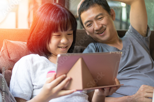 Father and daughter activity technology together concept. Asia kid girl reading or playing game on computer tablet with dad having fun and good time.