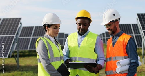 Portrait of electrician engineers in safety helmet and uniform checking solar panels. Group of three engineers at solar station.