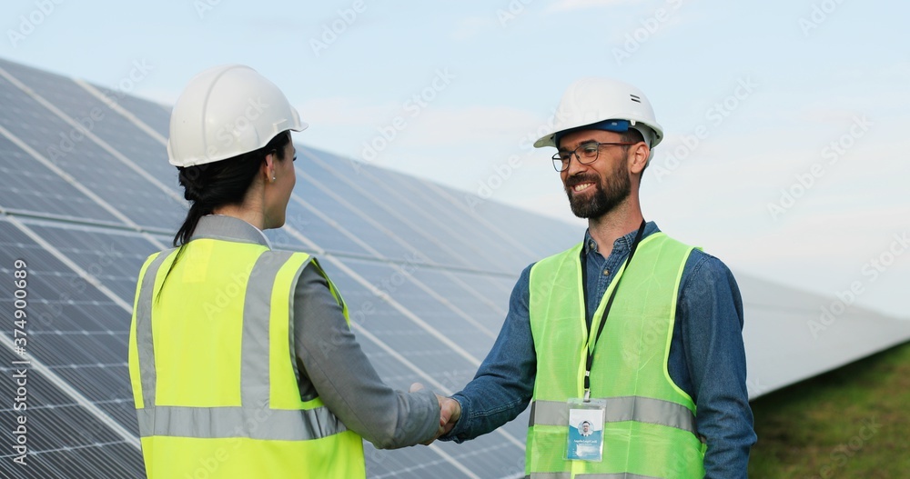 Portrait of two engineers in safety helmet and uniform shaking hands after discussion on background of photovoltaic solar panels. Portrait of two engineers in safety helmet and uniform shaking hands after discussion on background of photovoltaic solar panels.