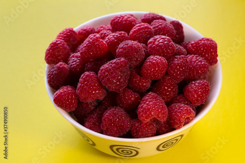 Raspberries in a white plate on a yellow background.