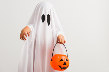 Funny Halloween Kid Concept, little cute child with white dressed costume halloween ghost scary he holding orange pumpkin ghost on hand, studio shot isolated on white background