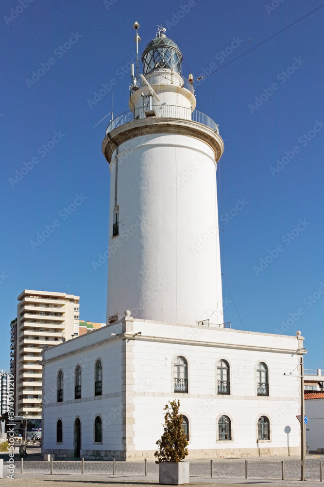 Malaga, Spain - January 17, 2019: bright white lighthouse on a sunny winterday against a blue sky. Malaga, Spain - January 17, 2019: bright white lighthouse on a sunny winterday against a blue sky.