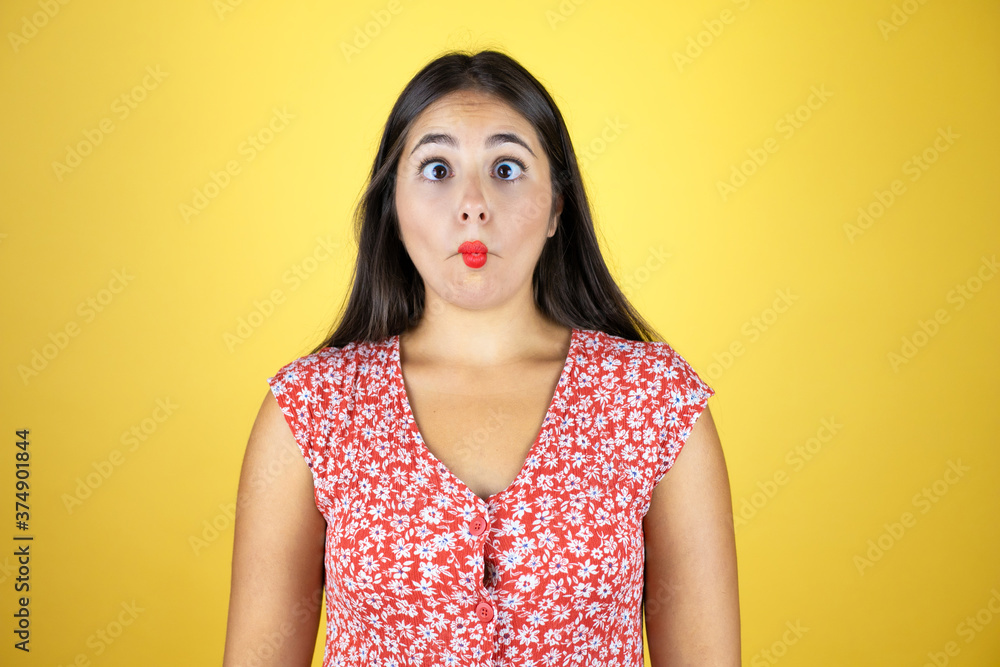 Young beautiful woman over isolated yellow background making fish face with lips, crazy and comical gesture. Young beautiful woman over isolated yellow background making fish face with lips, crazy and comical gesture.