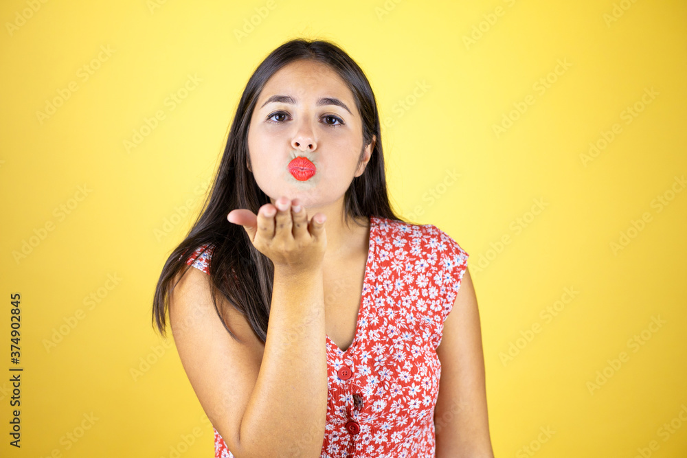 Young beautiful woman over isolated yellow background looking at the camera blowing a kiss with hand on air being lovely and sexy. Love expression. Young beautiful woman over isolated yellow background looking at the camera blowing a kiss with hand on air being lovely and sexy. Love expression.