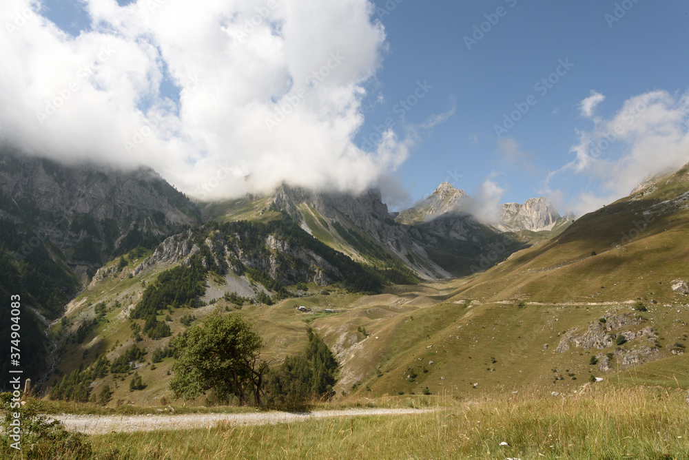 landscape of the mountain peaks of the Alps, rugged and rocky mountains, part of the French Alps mountain range. The sky between clear blue, is covered with white clouds, you can see in the valley the