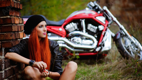 Portrait of charming young woman with red hair near a motorcycle