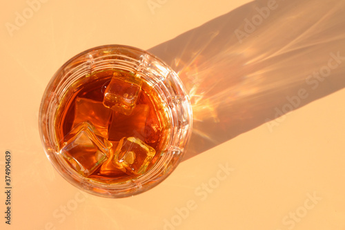Glass of cold whiskey on beige background with sunny shadow.