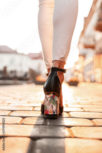 Female legs in white jeans in elegant leather sandals walks in the city at sunset. Top view