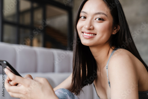 Image of happy asian woman using mobile phone while sitting on floor Free Download Image of happy asian woman using mobile phone while sitting on floor - GFXLoad