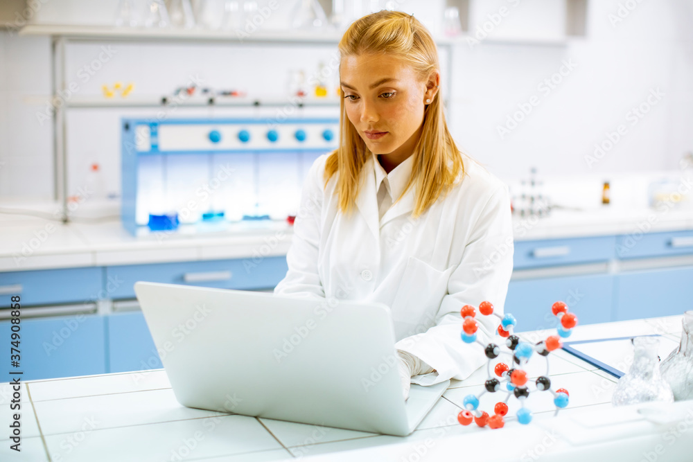 Female researcher in white lab coat using laptop while working in the laboratory Female researcher in white lab coat using laptop while working in the laboratory