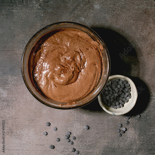 Dough for home baking classic dessert brownies in glass bowl, with chocolate chips over grey texture background. Flat lay, space