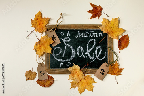 Autumn sale concept. Vintage chalkboard with hand written lettering Sale, labels with percents, yellow autumn leaves over beige background. Flat lay.
