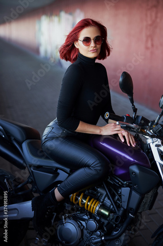 A girl with red hairs posing with dark urban motorcycle