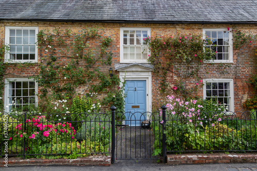 The exterior of an english cottage with flowers blooming in the front garden and sash windows, A typical english countryside cottage