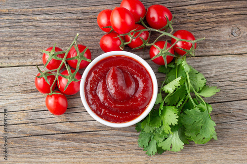 White bowl of tomato sauce with parsley and tomato. Ketchup on natural wooden background