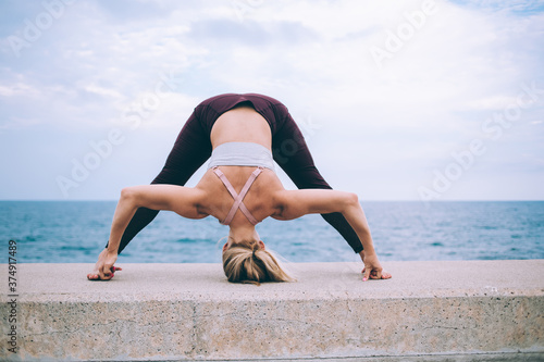Experienced female trainer practicing Prasarita Padottanasana exercise during morning active workout for mindfulness, slim woman enjoying pilates warm up at nature and free time for hatha yoga