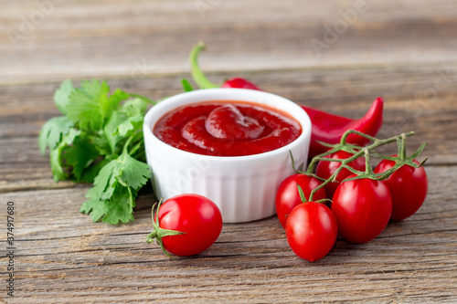 White bowl of tomato sauce with parsley pepper and tomato. Ketchup on natural wooden background