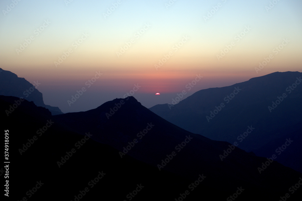 Silhouettes of mountains in the morning haze. The sun rises over the mountains.