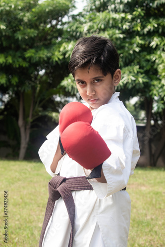 Sporty Asian Indian Kid Posing With Boxing Gloves And Aggression In Eyes Wearing White Karategi Kimono
