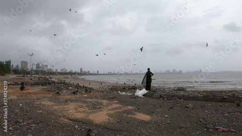 Lady At The Nearly Empty Beach With Flying Birds And City At The Background During Corona Virus Pandemic In Mumbai, India. - Wide Shot photo