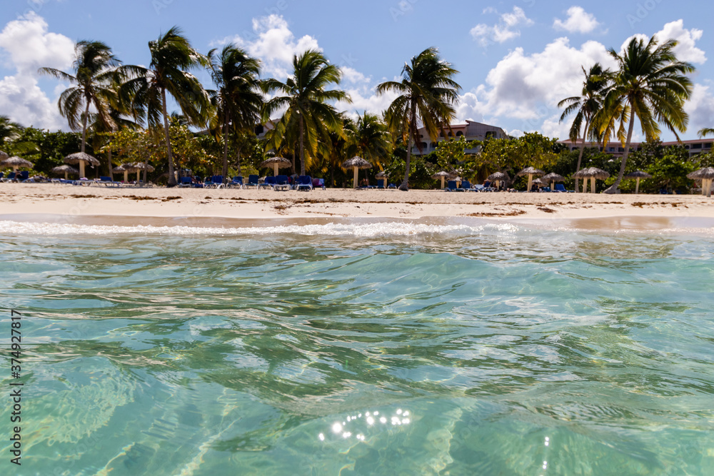 Obraz premium View from the blue water to the tropical beach of Cuba with sand and a lot of palms