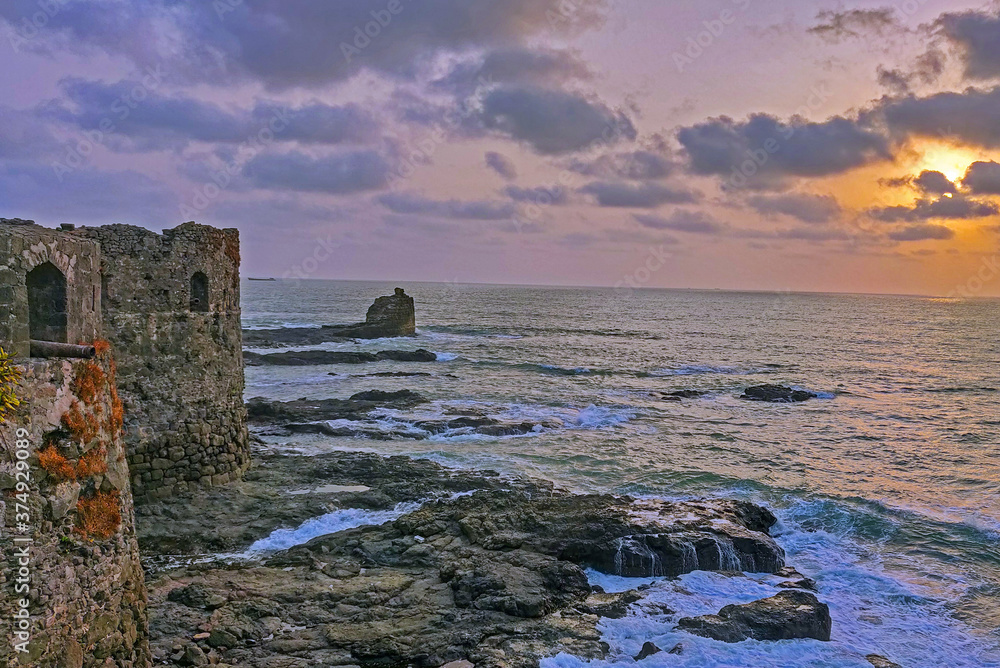 A beautiful landscape showing blue and orange light during sunset hours. Tides are hitting the walls of sea fort. The entire frame looks like a perfect wallpaper. Grey rock adding more crisp in frame
