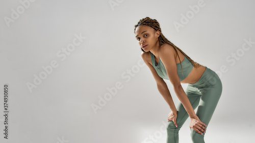 Work hard. Tired exausted athletic mixed race woman in sportswear resting after workout while standing isolated over grey background photo