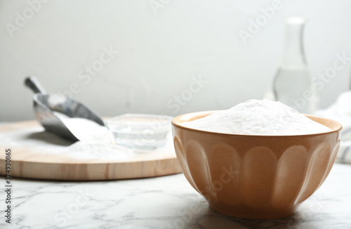 Baking soda in bowl on white marble table. Space for text