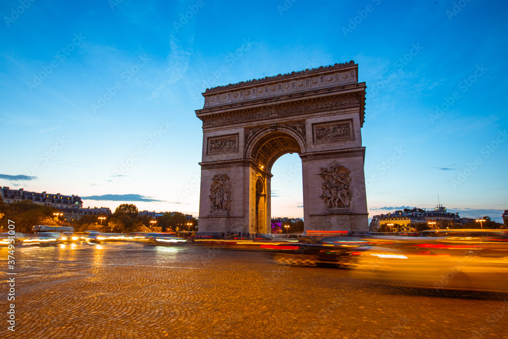 The night view of triumphal arch and traffic in Paris, France.