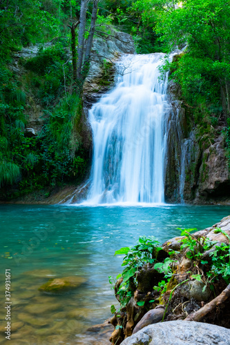 A large beautiful waterfall in a forest with blue water and a trees. © Oksana