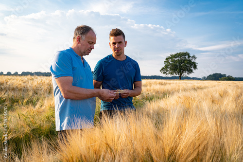Ackerbau - Landwirt  steht beim Sonnenuntergang mit seinem Sohn in einem goldgelben Getreidefeld