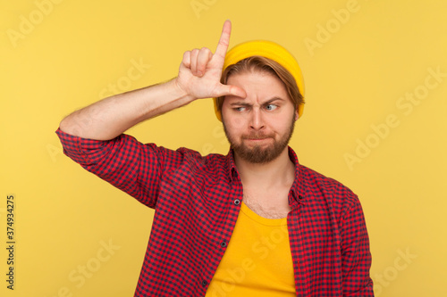 Obraz na plátně I am so unlucky! Depressed hipster guy in beanie hat and checkered shirt showing L sign, loser gesture on forehead, looking sorrowful frustrated, upset over defeat